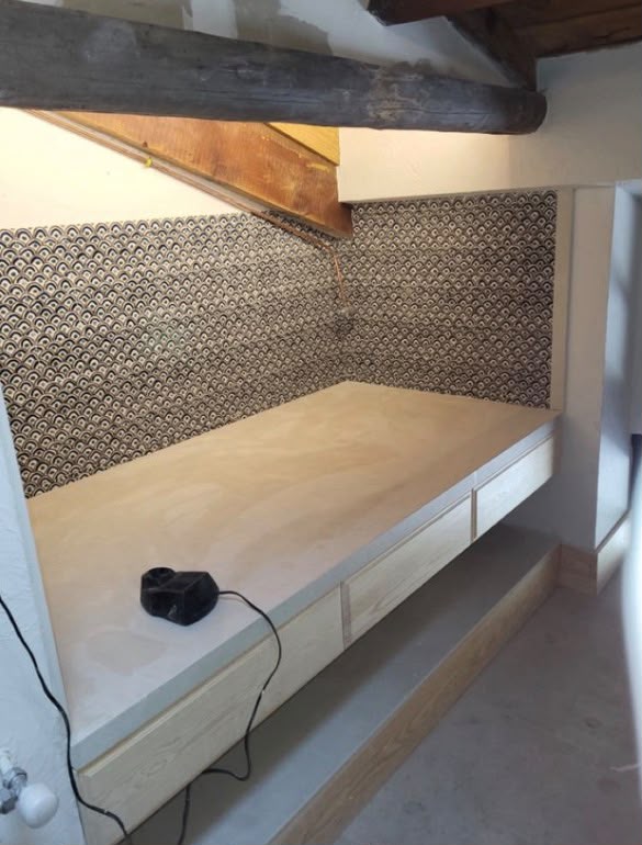 Dormitorio abuhardillado reformado con cama de obra, cajones a medida y alicatado decorativo